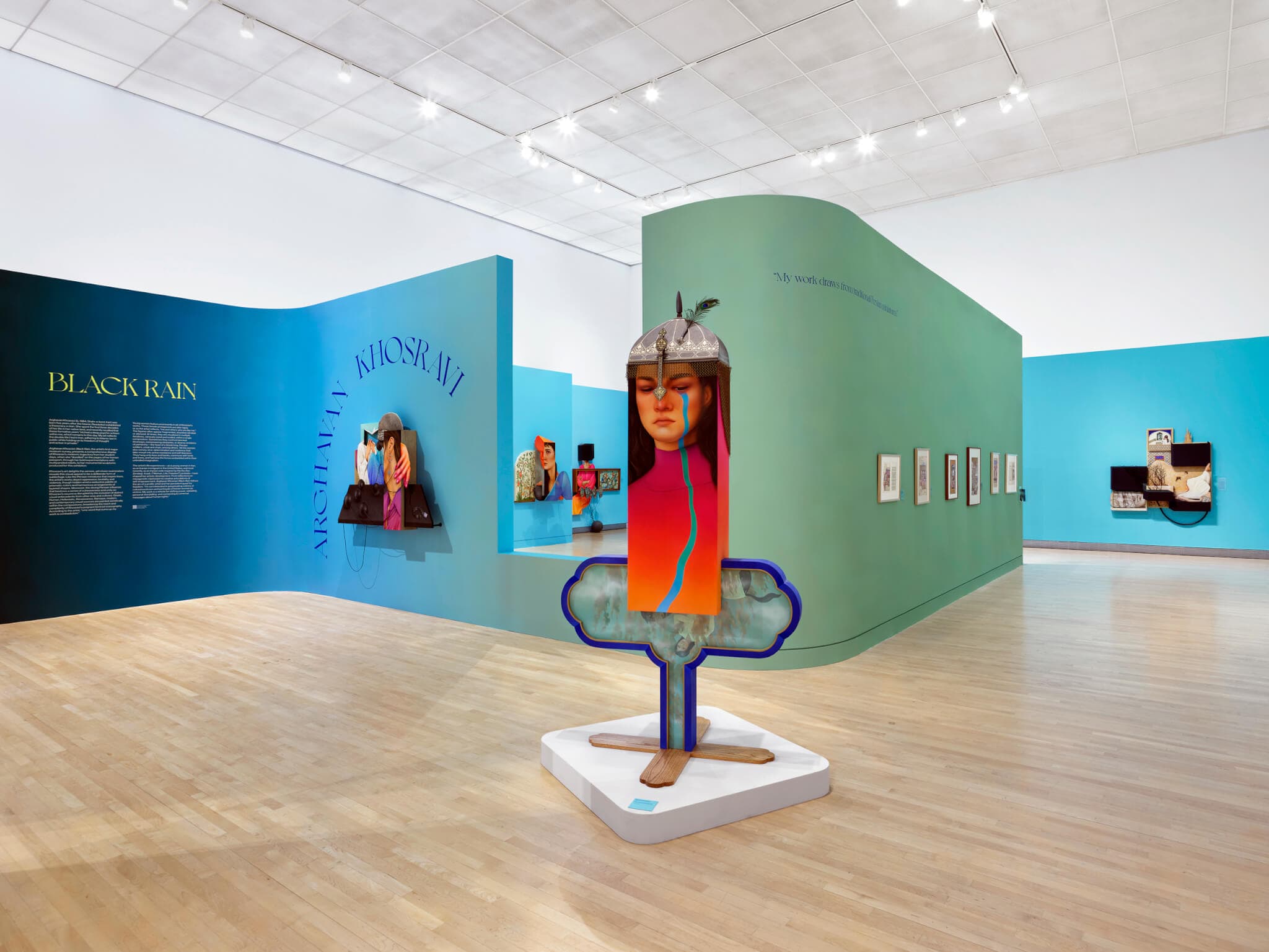 The face of a woman emerges as part of a sculpture in the center of a room, set in front of blue and green walls.