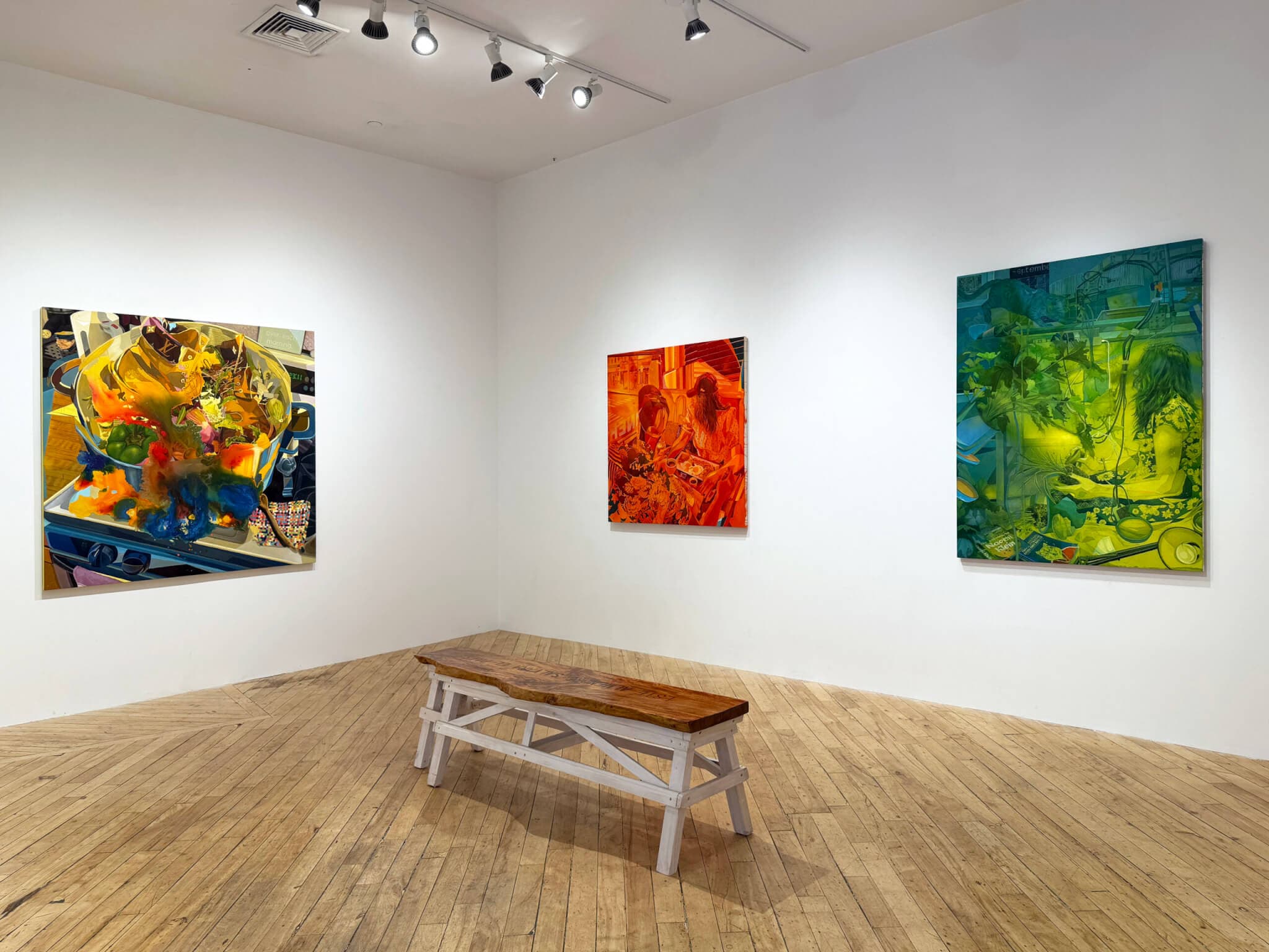Three paintings in bright hues hang on gallery walls. A bench is placed in the middle of the wooden floor.